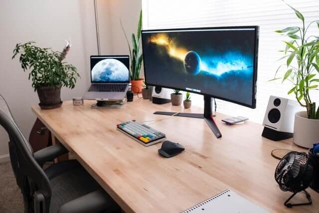 Arbeitsplatz am Holzschreibtisch mit Monitor, Laptop und Pflanzen